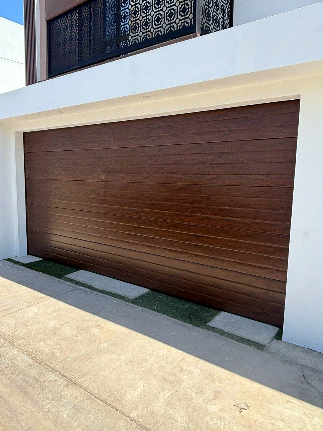 Puerta seccional madera oscura instalada en fachada blanca